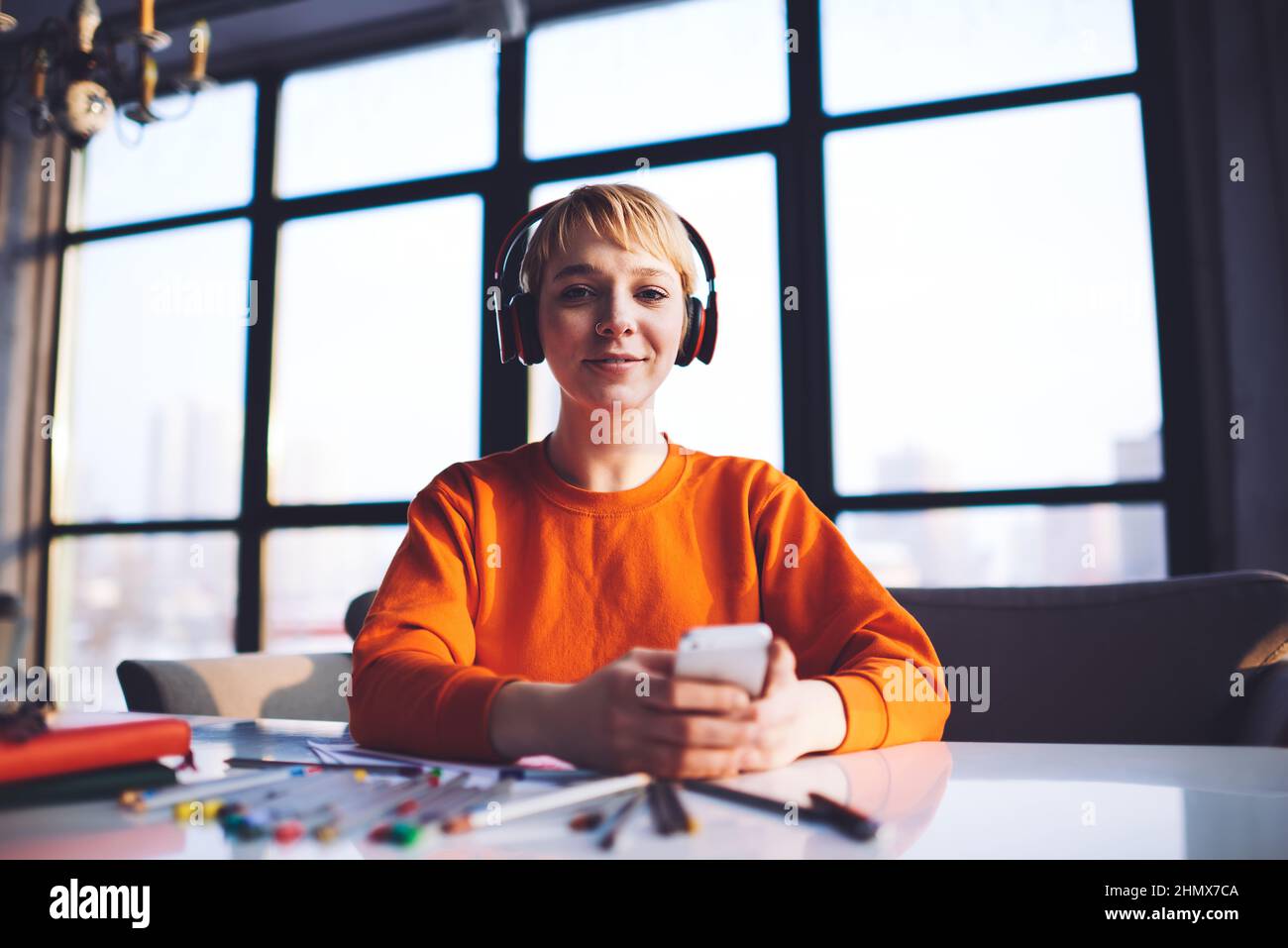 Giovane designer che ascolta la canzone utilizzando lo smartphone lavorando a progetti creativi Foto Stock