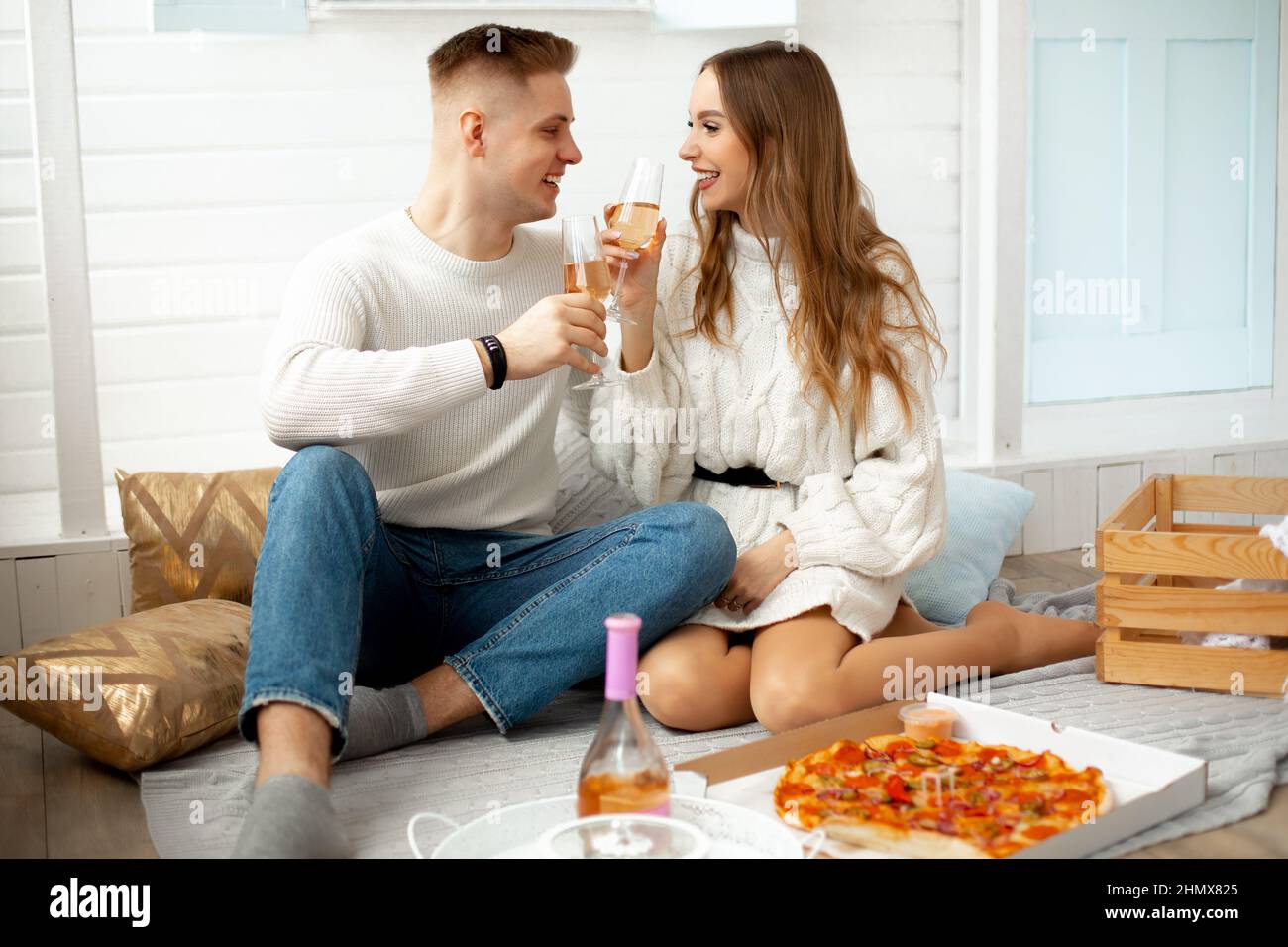 Felice insieme. Bei giovani hanno organizzato data con pizza e vino a casa, si siedono sul pavimento contro il muro bianco e portare bicchieri di vetro a Foto Stock