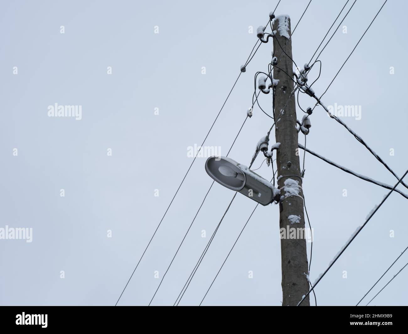 Un vecchio palo di legno elettrico con una lampada e cavi elettrici appesi su di esso e un po' di neve su di esso. Primo piano. Foto Stock
