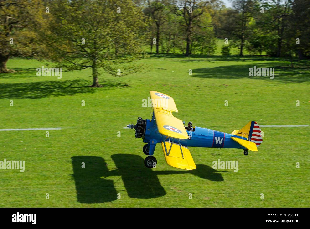 Boeing Stearman biplanare N4712V, aereo trainer che decollo da Henham Park campagna erba striscia. Pista alberata in erba Suffolk nella soleggiata giornata estiva Foto Stock