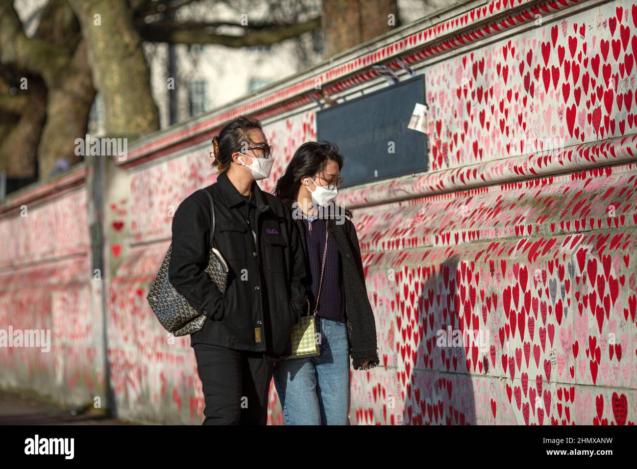Due turisti asiatici con maschera guardando il National COVID Memorial Wall dipinto con cuori rossi in bella giornata di sole. Westminster, Londra , Regno Unito Foto Stock