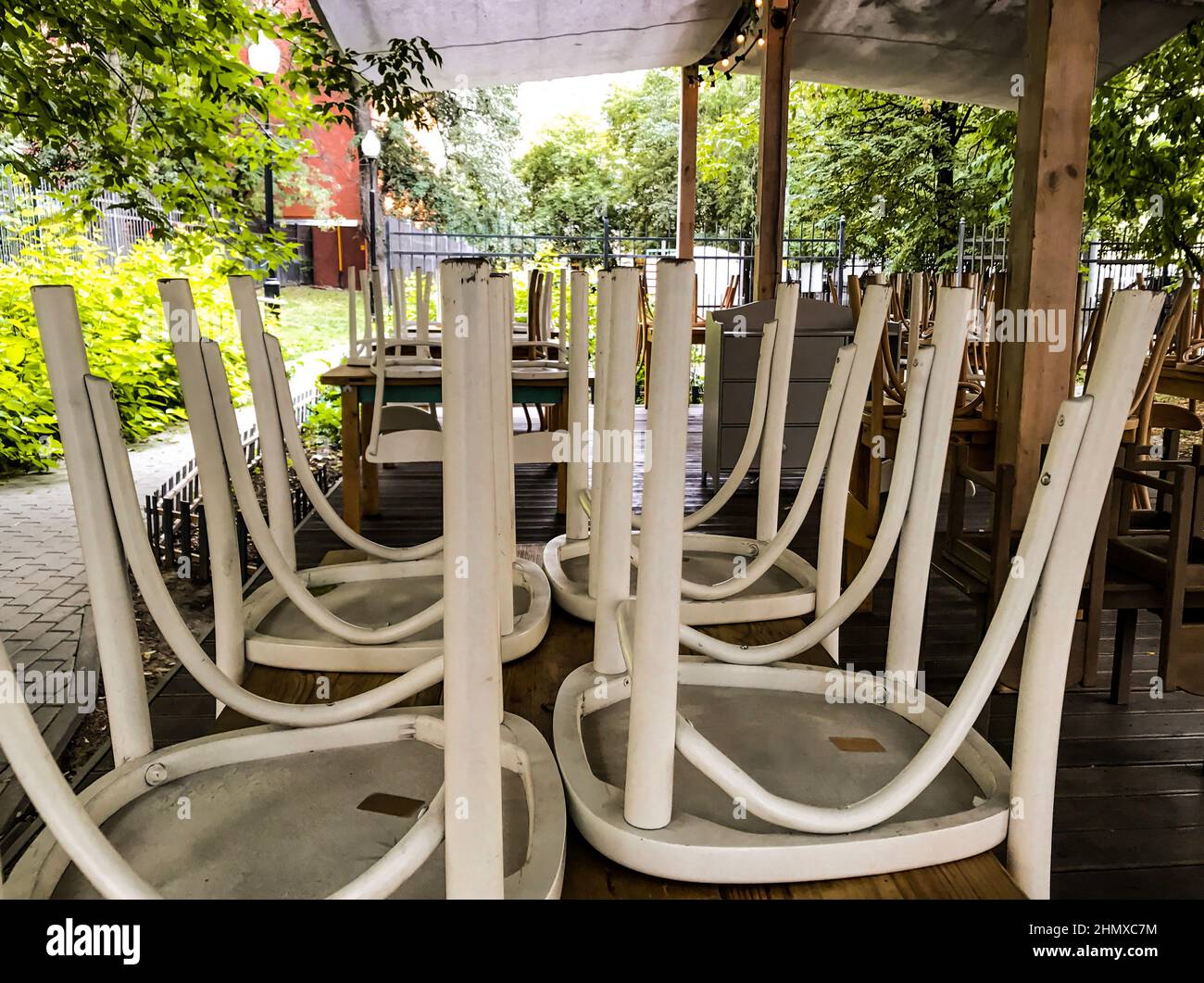 La terrazza estiva in legno del caffè è chiusa, non ci sono persone, le sedie sono ribaltate, alberi verdi sono tutto intorno. Foto Stock