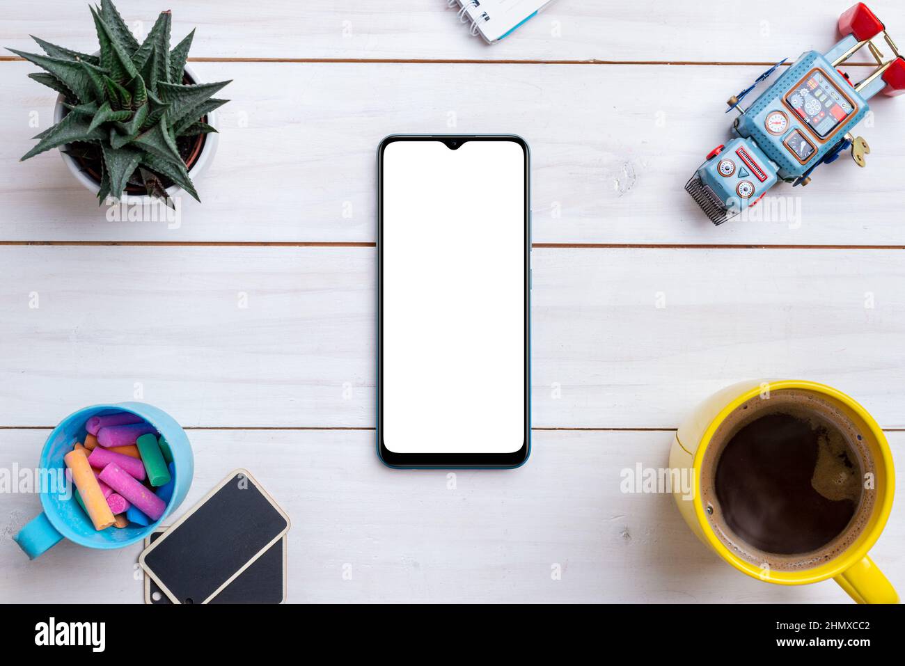 Tavolo da lavoro creativo a disposizione piatta con mockup smartphone circondato da giocattolo robot, tazza di caffè, piante e gesso colorato Foto Stock