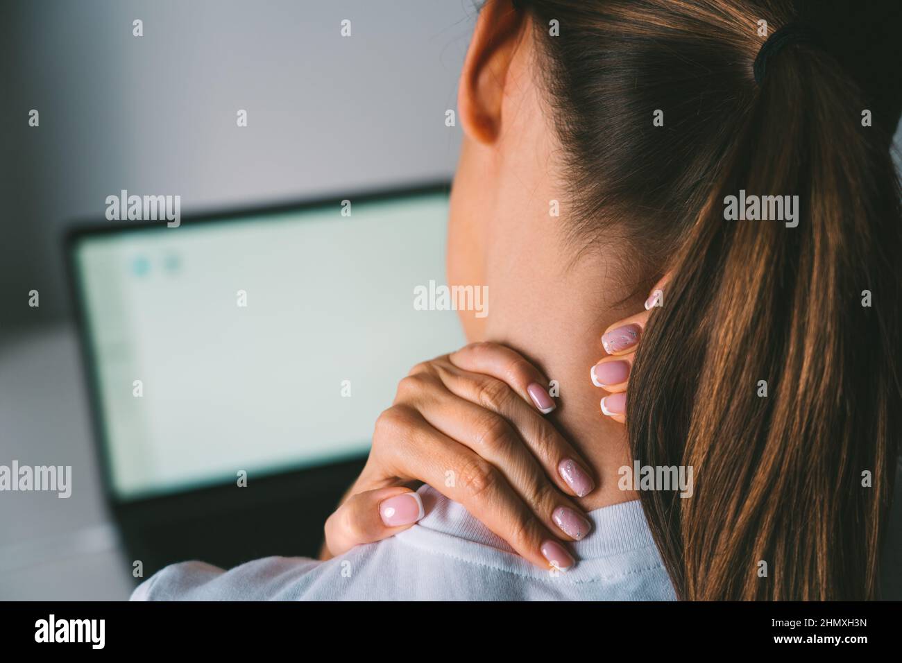 Donna che massaggiava il collo per alleviare il dolore al collo dopo aver lavorato sul laptop Foto Stock