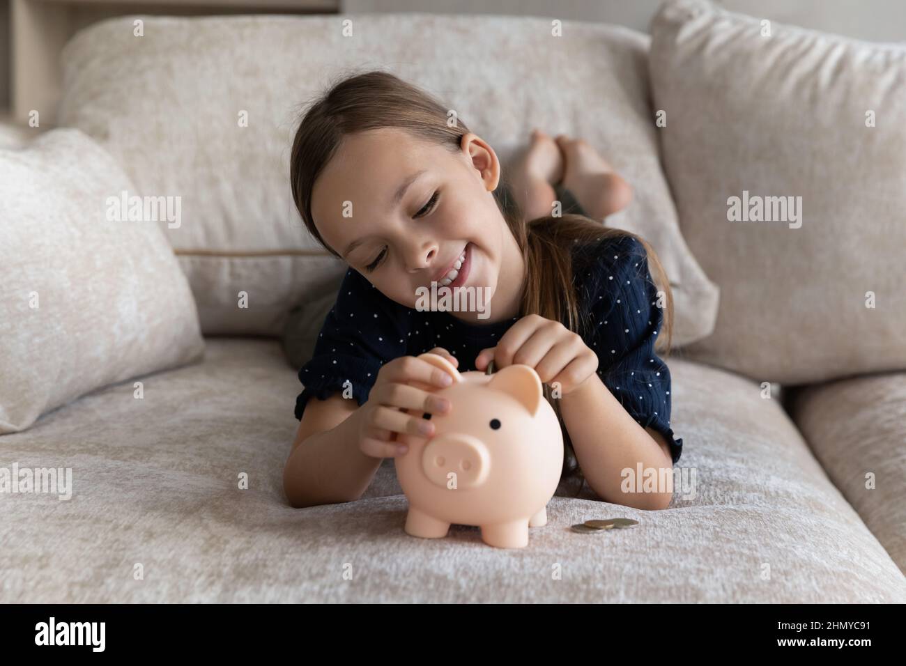 Bambino felice che raccoglie i soldi, gettando le monete nella banca del piggy Foto Stock