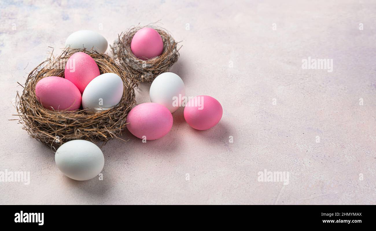 Uova rosa tenue e bianche pastello in un nido e su uno sfondo chiaro. Vista laterale, spazio di copia. Il concetto di Buona Pasqua. Foto Stock