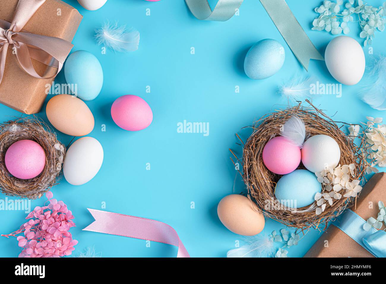Sfondo pasquale con uova colorate, nidi, nastri e piume su sfondo blu. Vista dall'alto, spazio di copia. Buona Pasqua. Foto Stock