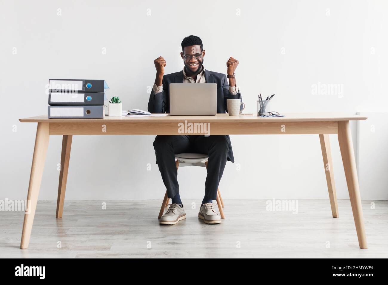 Il millenario impiegato dell'ufficio afro-americano seduto alla scrivania con un laptop, fa sì gesto contro la parete bianca Foto Stock