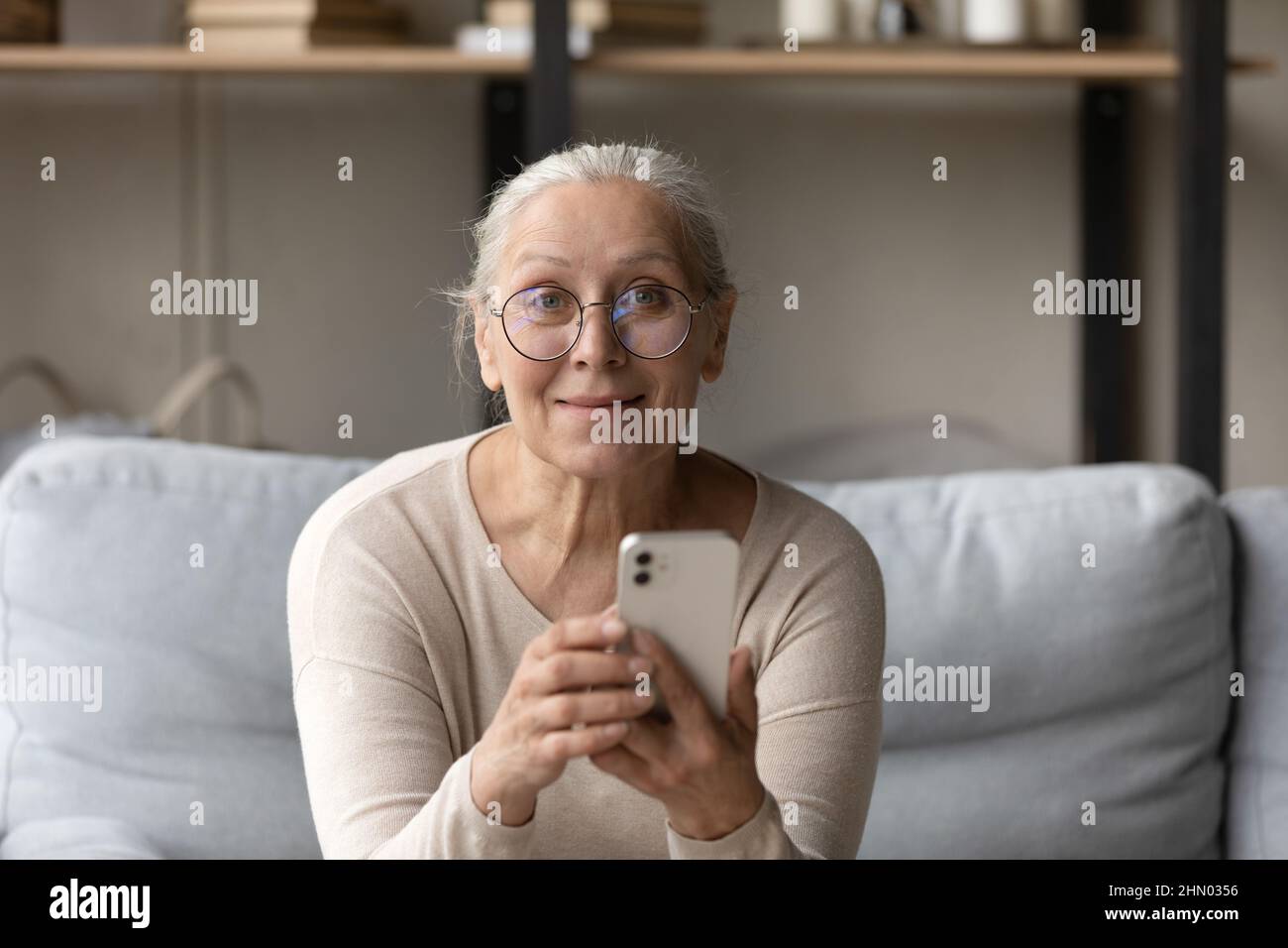 Felice ragazza più anziana allegra in eyewear tenendo smartphone Foto Stock