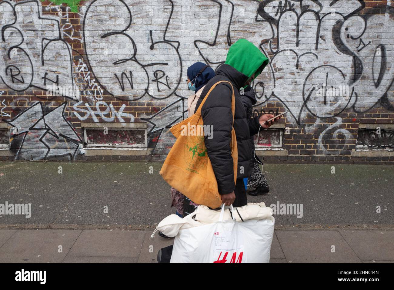 Tre persone si fanno strada davanti a un muro di graffiti sulla Bethnal Green Road nella East London UK Foto Stock
