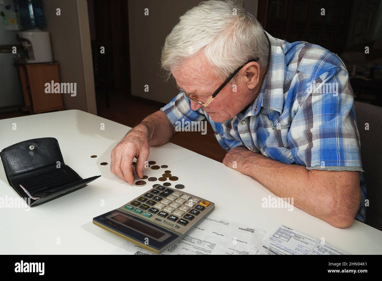 Sconvolto uomo anziano seduto al tavolo e calcolando le finanze. Vecchio controllo fatture. Uomo che conta le monete sul tavolo. Concetto di calcolo della pensione Foto Stock