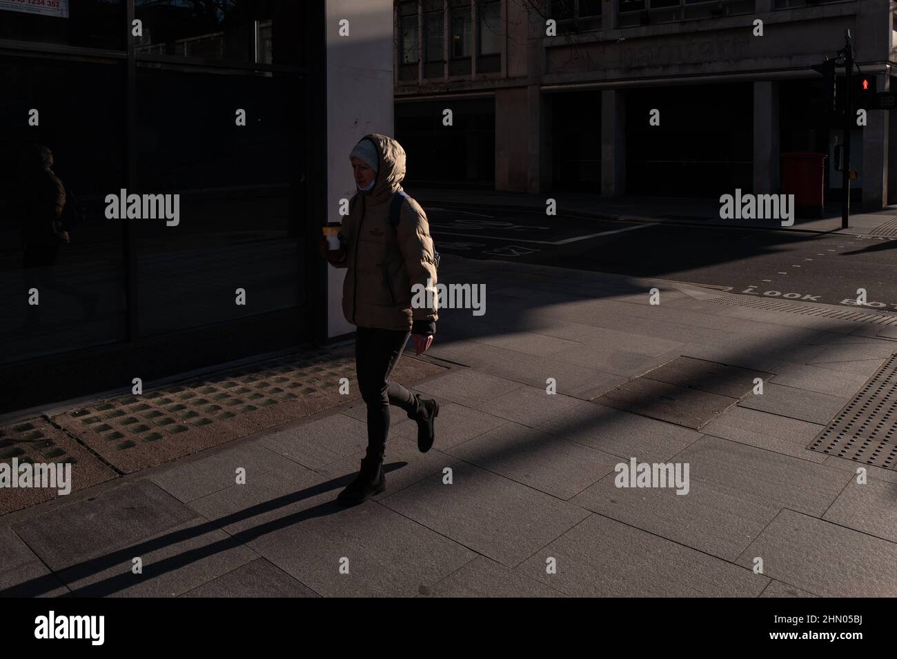 Una persona da sola si fa strada lungo Tottenham Court Road in una mattinata soleggiata ma fredda gustando una bevanda calda. Foto Stock