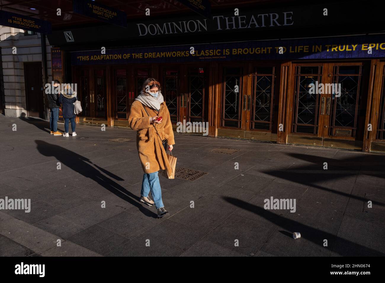 Una donna passa davanti al Dominion Theatre nel West End di Londra in una mattinata invernale allegra ma fredda. Londra, Regno Unito Foto Stock