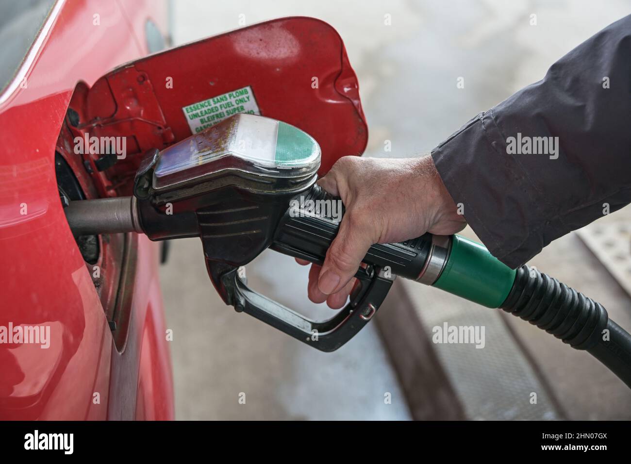 Mano di un uomo sta riempiendo la sua auto rossa con benzina alla stazione di benzina nonostante i prezzi in aumento, concetto di crisi energetica e necessità di comportamento sostenibile fo Foto Stock