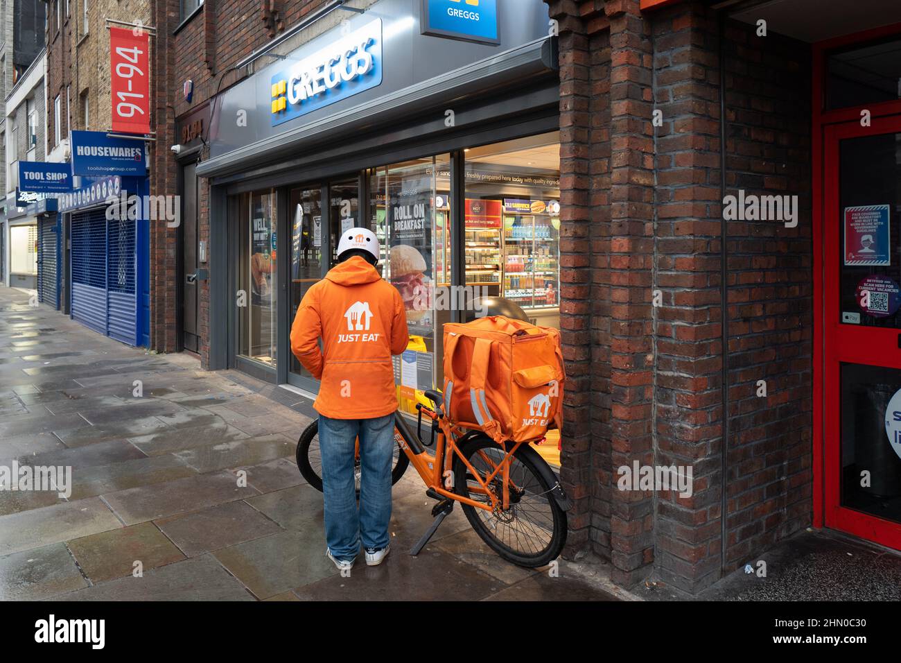 Una persona di consegna di Just Eat si prepara ad entrare in Greggs per ritirare un ordine per la consegna. Preso presto la Domenica mattina a Lower Marsh, Waterloo Londra Foto Stock