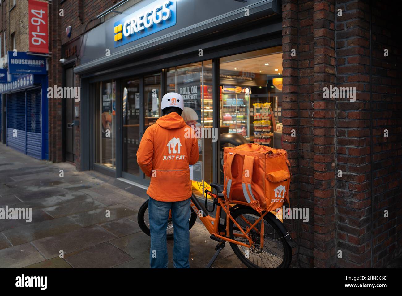 Una persona di consegna di Just Eat si prepara ad entrare in Greggs per ritirare un ordine per la consegna. Preso presto la Domenica mattina a Lower Marsh, Waterloo Londra Foto Stock