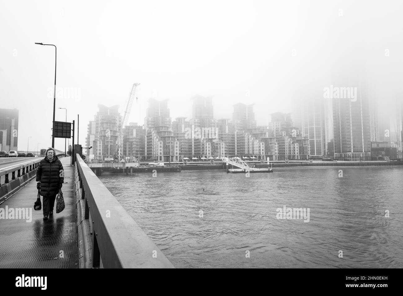 Una donna attraversa Vauxhall Bridge in una mattinata umida a Londra nel Regno Unito. In background le case moderne e le attrezzature di costruzione possono essere osservate Foto Stock