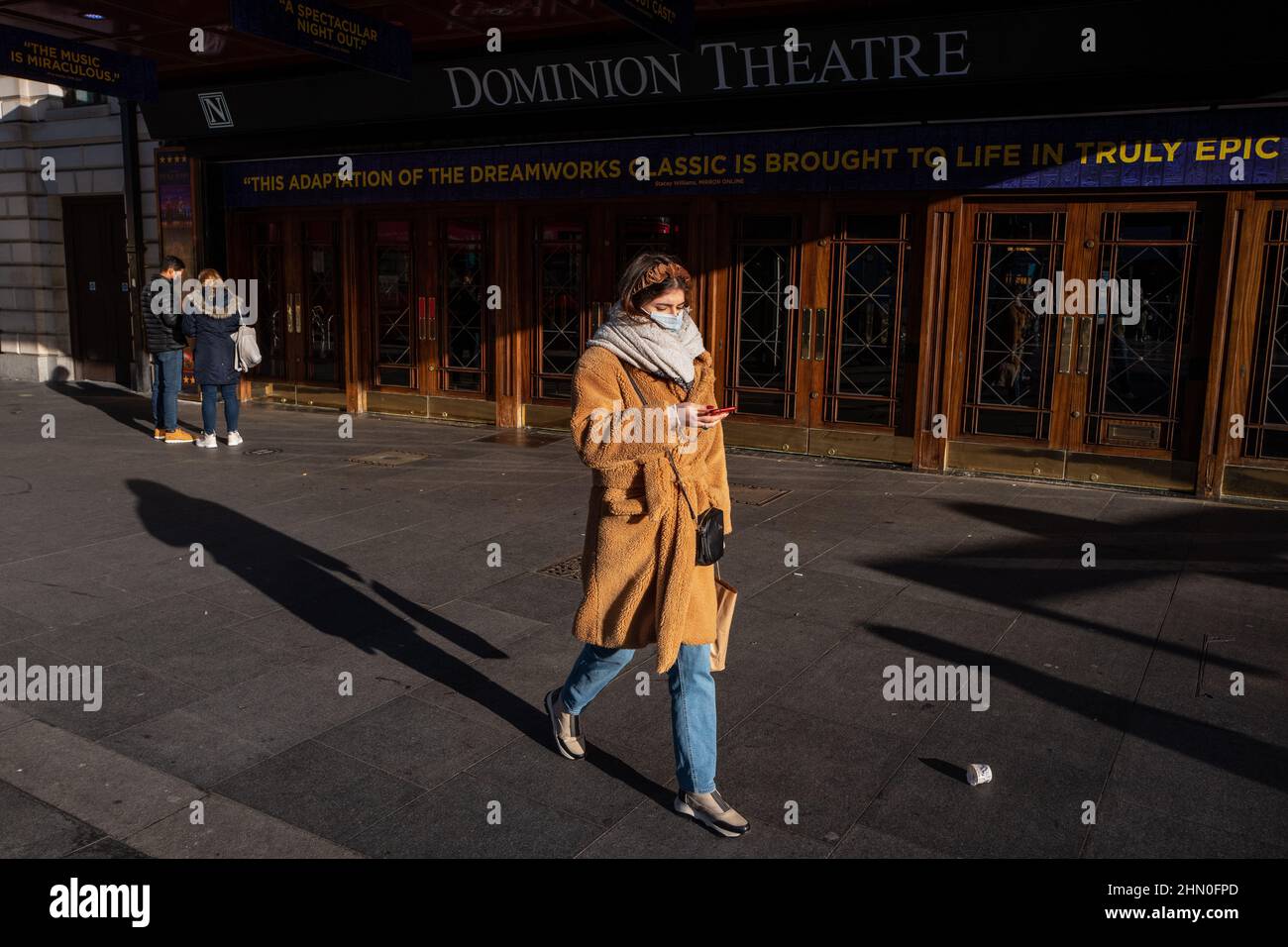 Una donna passa davanti al Dominion Theatre nel West End di Londra in una mattinata invernale allegra ma fredda. Londra, Regno Unito Foto Stock