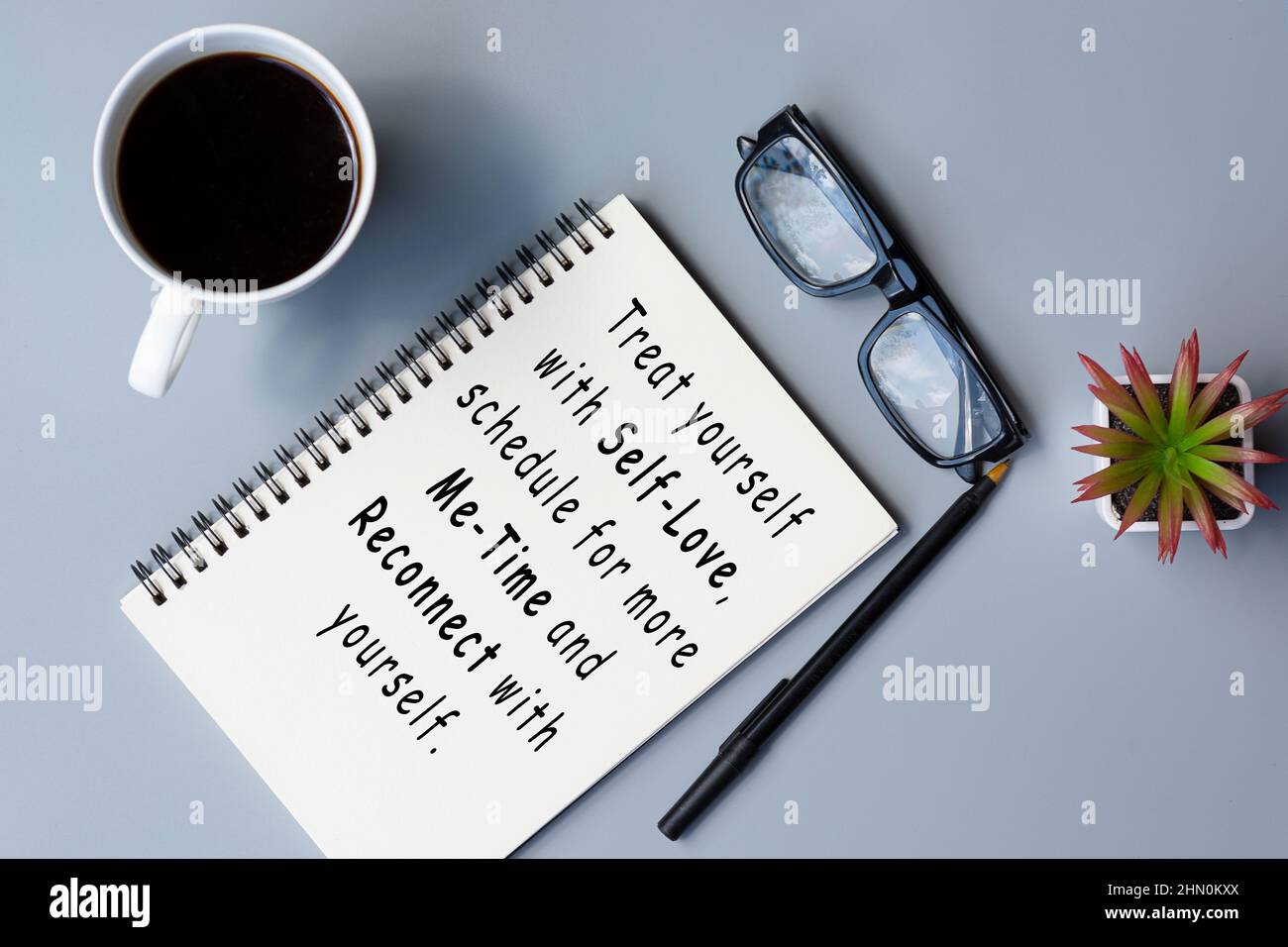 Citazione motivazionale su blocco note con caffè e bicchieri da lettura su una scrivania. Foto Stock