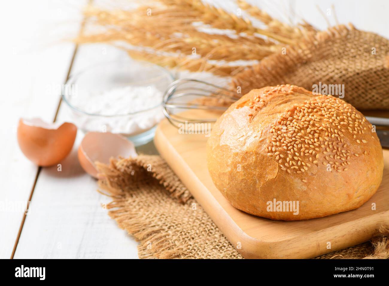 Pane di pasta madre con Sesame su legno placcato e sussurro, farina e gusci d'uovo su sfondo di legno bianco, concetto di panetteria fatta in casa. Foto Stock