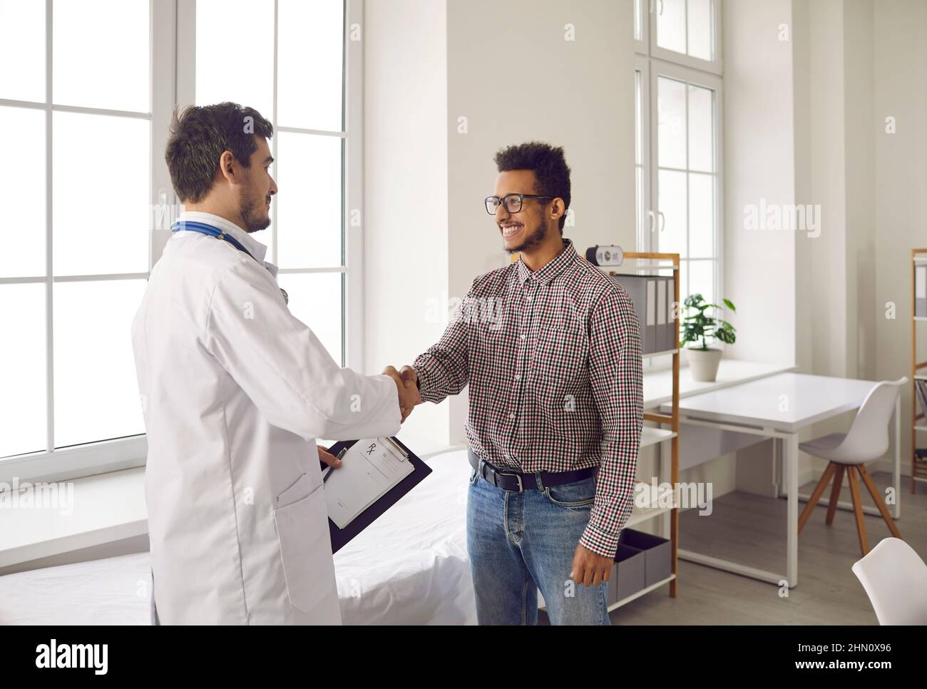 Il giovane medico giovane e amichevole scuote le mani e saluta il paziente nella clinica medica moderna. Foto Stock