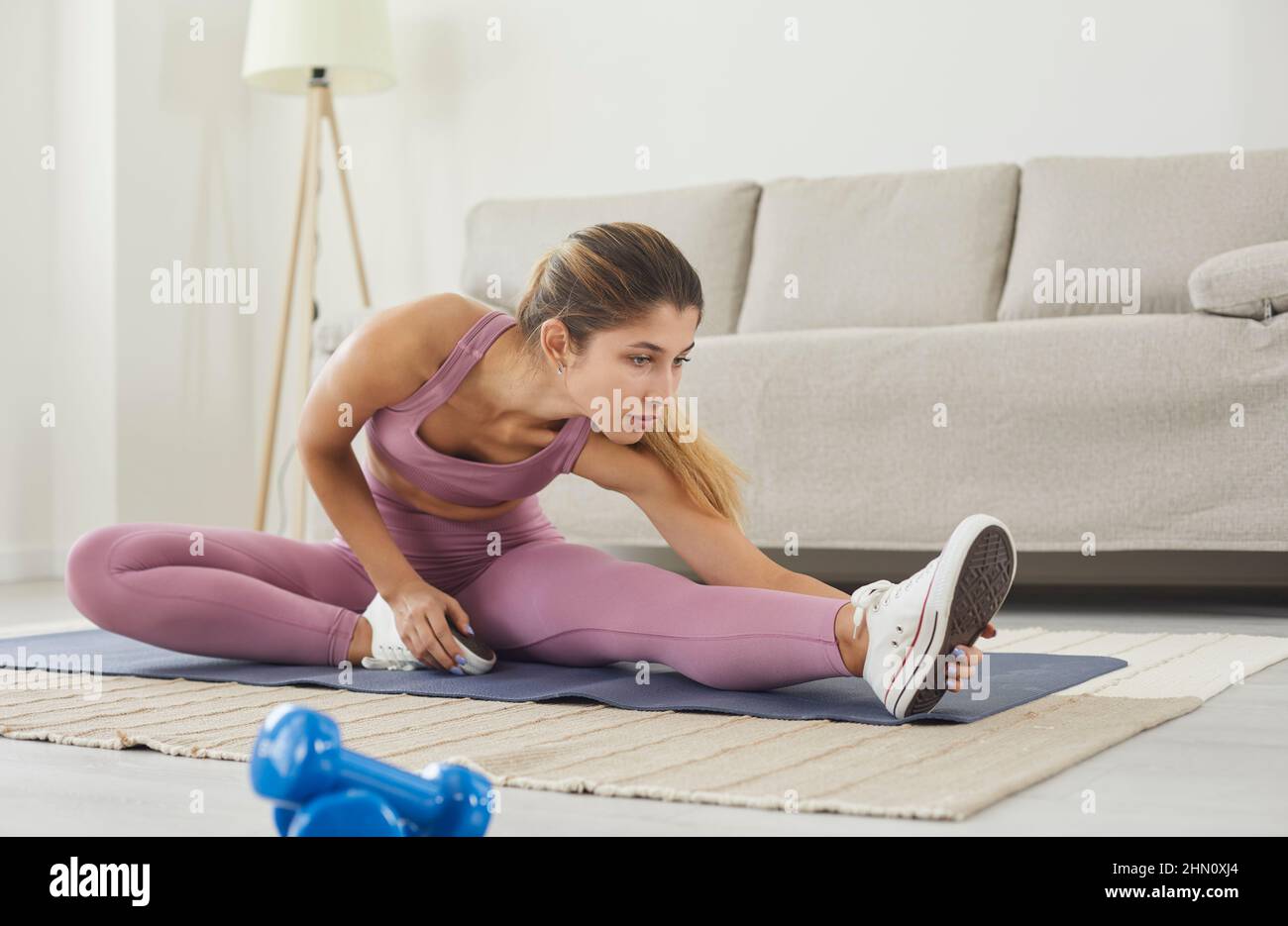 Donna con alta flessibilità del corpo che allunga la gamba per riscaldarsi facendo esercizi di ginnastica aerobica. Foto Stock