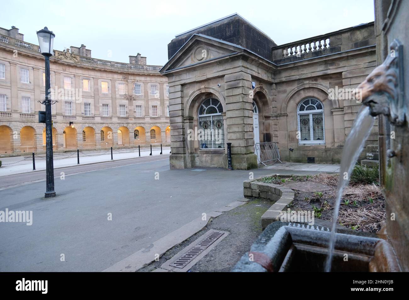 L'acqua potabile di sorgente di Buxton emana dalla fontana della testa del leone presso il pozzo di St Ann's con l'hotel Buxton Crescent e la Pump Room sullo sfondo Foto Stock