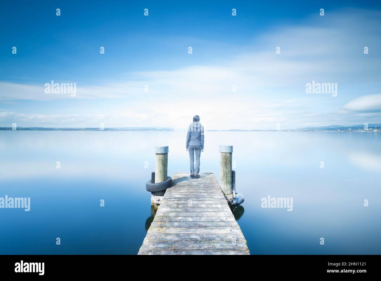 Doppia esposizione. Figura femminile su un molo di legno. La riva del lago, una lunga esposizione. Minimalismo, riflessione di sé, meditazione. Foto Stock