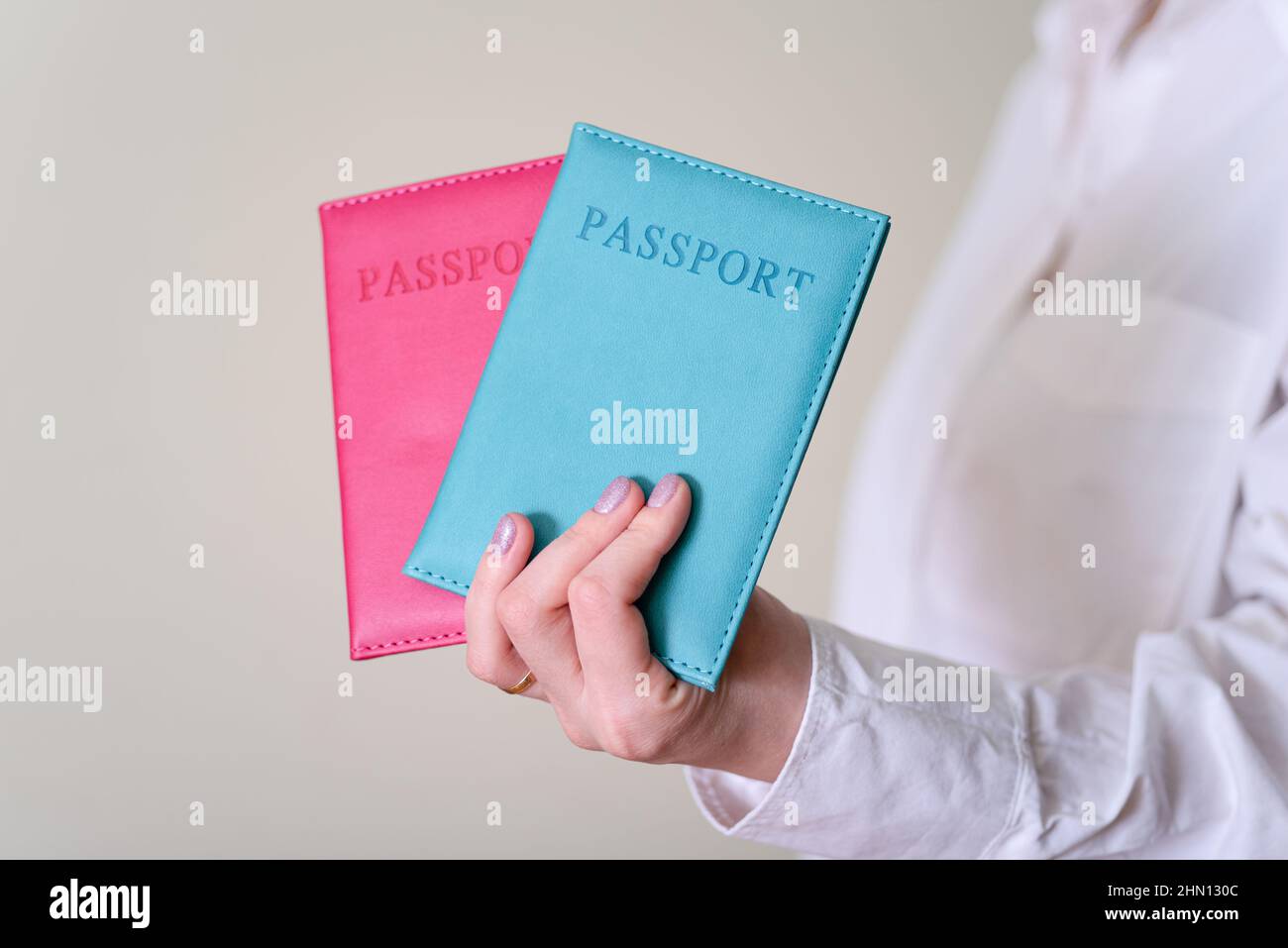 Una mano di donna che tiene due passaporti su sfondo grigio. Il concetto di viaggiare all'estero. Foto Stock