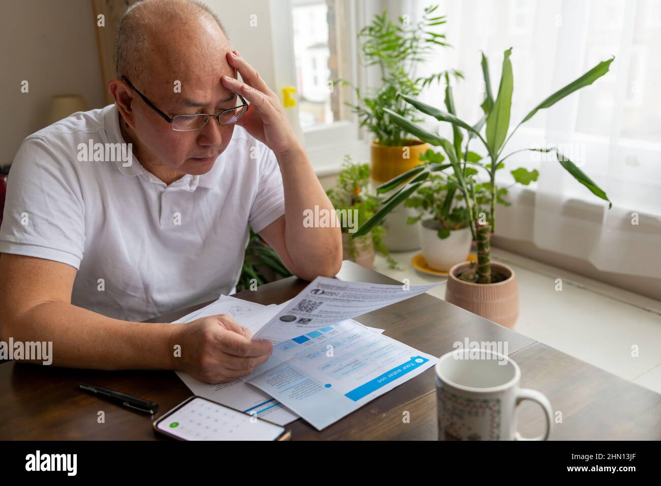 Un uomo anziano che tiene la sua testa cercando di far fronte al costo crescente di energia e tasse fatture. Foto Stock
