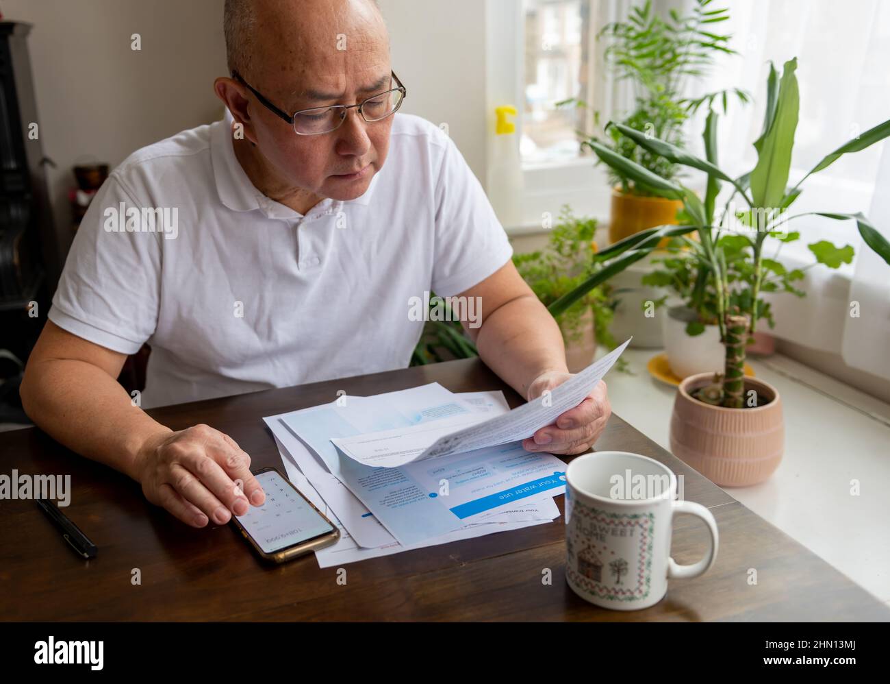 Un uomo anziano seduto da un tavolo che calcola il costo crescente di energia e tasse fatture. Concetto di inflazione e di costo di vita. Foto Stock