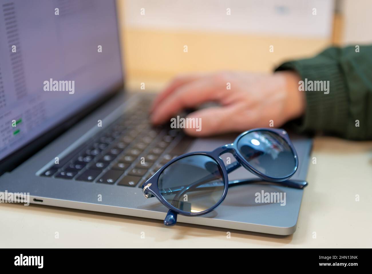 Una persona che utilizza un computer portatile con una mano sulla tastiera e un paio di occhiali da sole. Truffe online, cyber attacchi, concetto di frode. Foto Stock