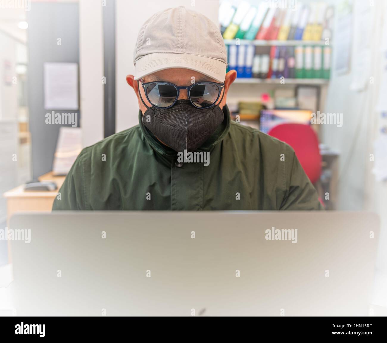 Una persona che indossa occhiali da sole, un cappuccio e una copertura per il viso utilizzando un computer portatile. Concetto di minaccia informatica, sicurezza e truffe finanziarie. Foto Stock