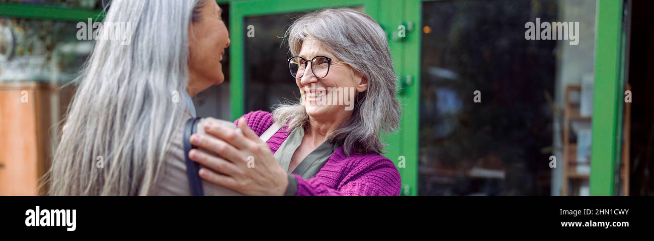 Una donna matura sorridente abbraccia l'incontro di amici femminili sulla strada moderna della città Foto Stock