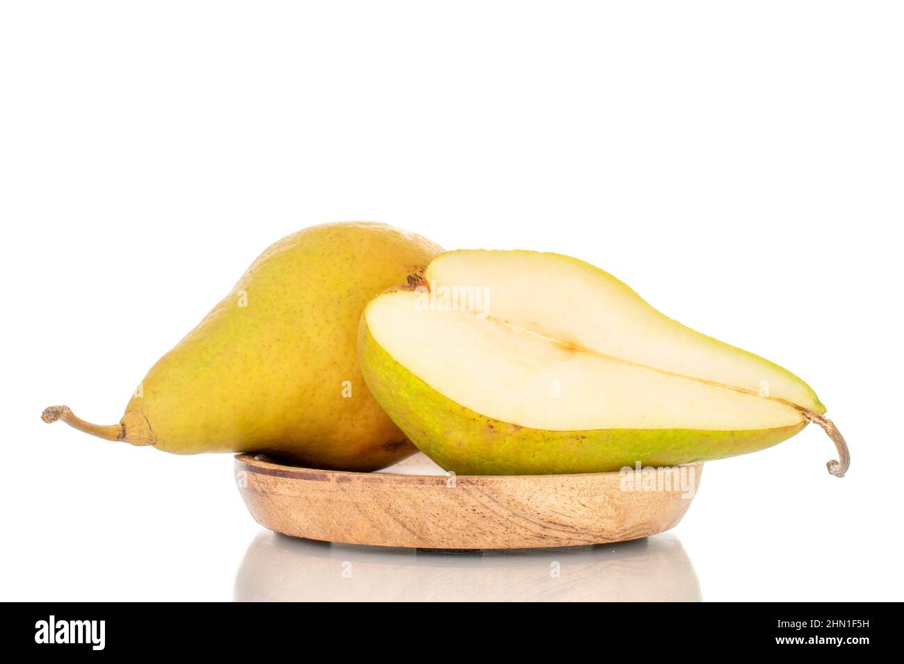 Una metà di pera dolce biologica e una intera pera su un piatto di legno, macro, isolato su bianco. Foto Stock