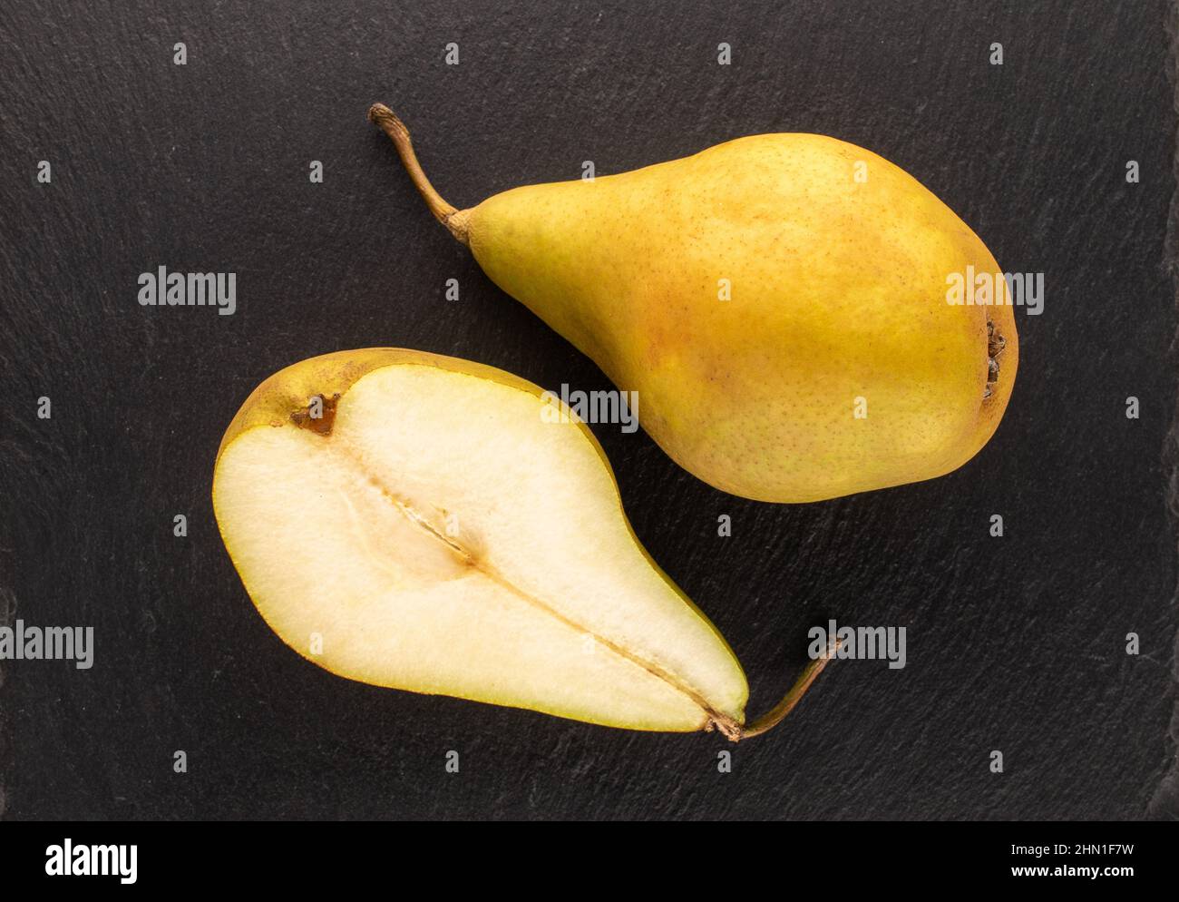 Una pera intera e una metà di una pera dolce biologica su una pietra ardesia, macro, vista dall'alto. Foto Stock