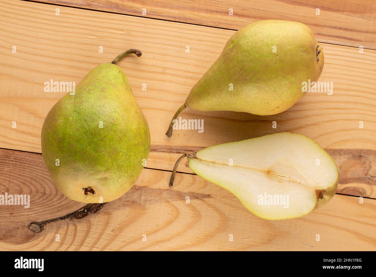 Due pere intere e una metà di una pera dolce biologica su un tavolo di legno, macro, vista dall'alto. Foto Stock