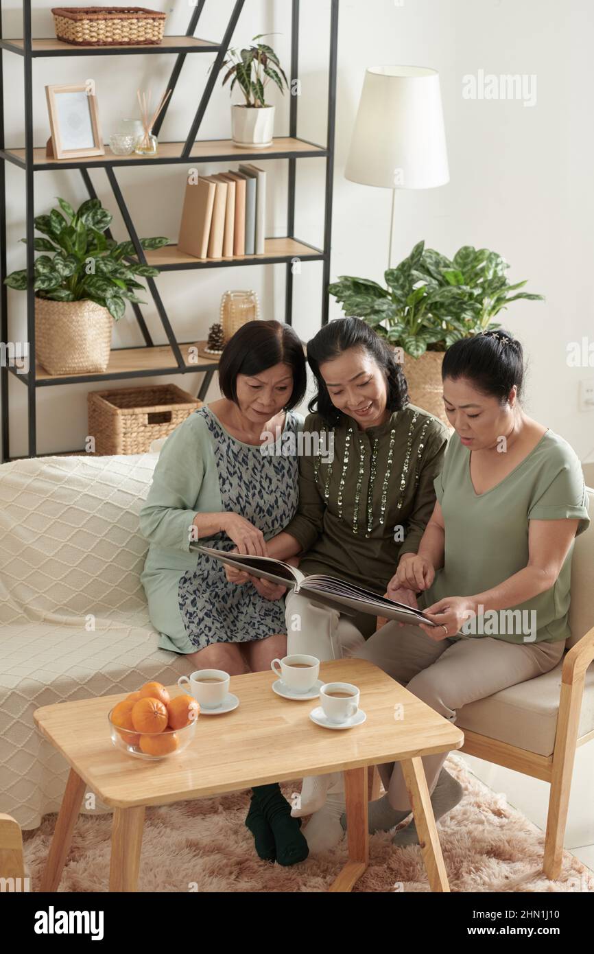 Amici senior femminili che guardano vecchie foto in album fotografico quando si riuniscono a casa per piccole feste Foto Stock