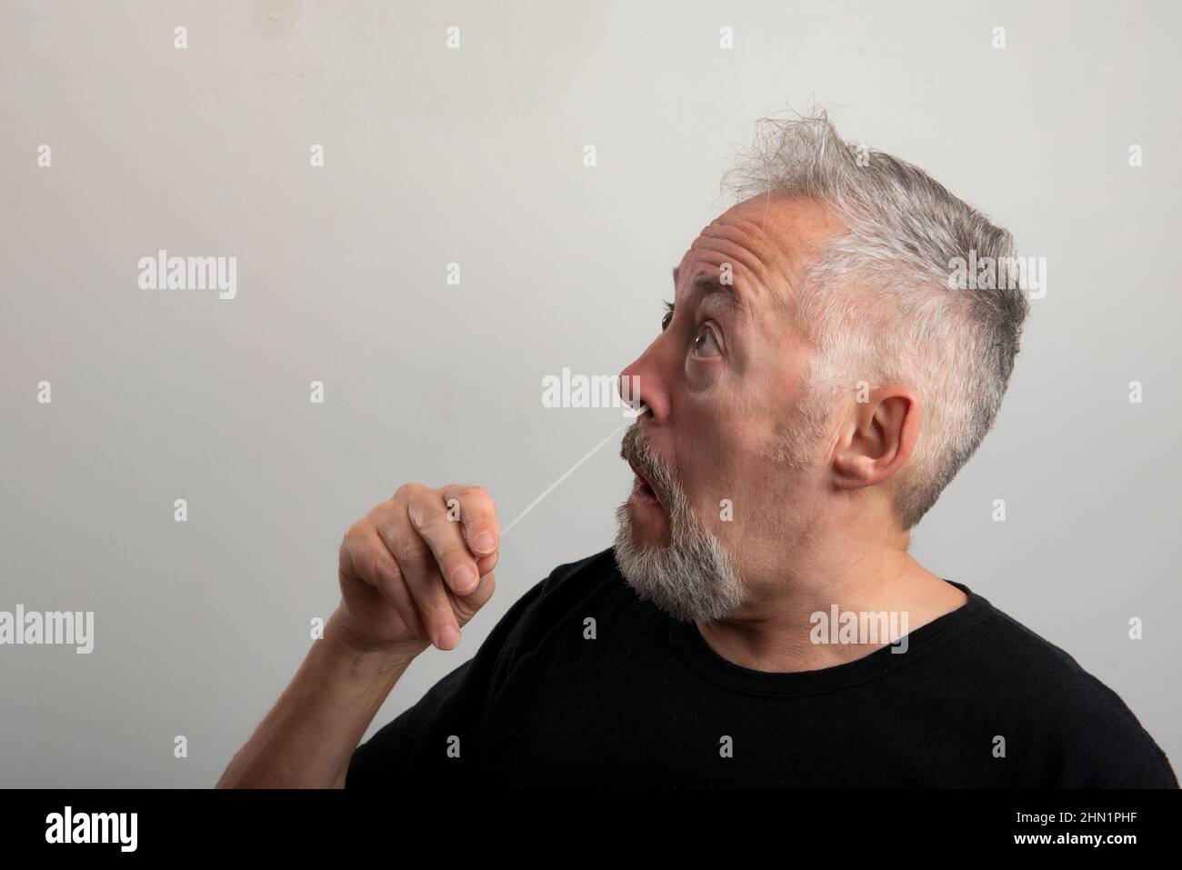 uomo di mezza età con capelli grigi e barba utilizzando il kit di auto-test rapido dell'antigene del coronavirus (covid-19) (atk) a casa con un tampone nasale di cotone Foto Stock