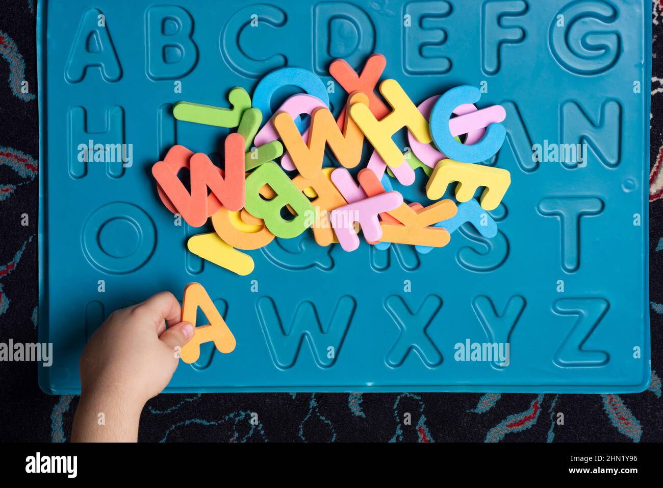 Una piccola mano del bambino che ordina le lettere spugnose colorate educative in foglio blu inciso, punto di vista superiore Foto Stock