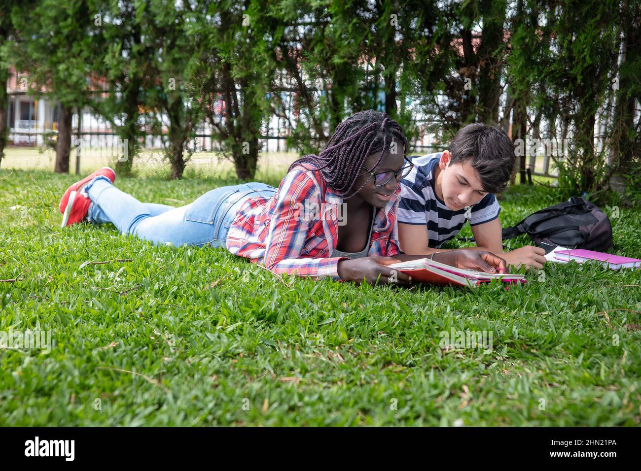 Scuola superiore caucasica e ragazzi africani coppia rilassarsi sdraiati sul prato in un parco pubblico Foto Stock