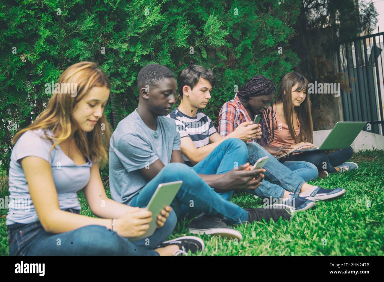 Studenti multietnici delle scuole superiori che si rilassano utilizzando gadget elettronici all'aperto Foto Stock