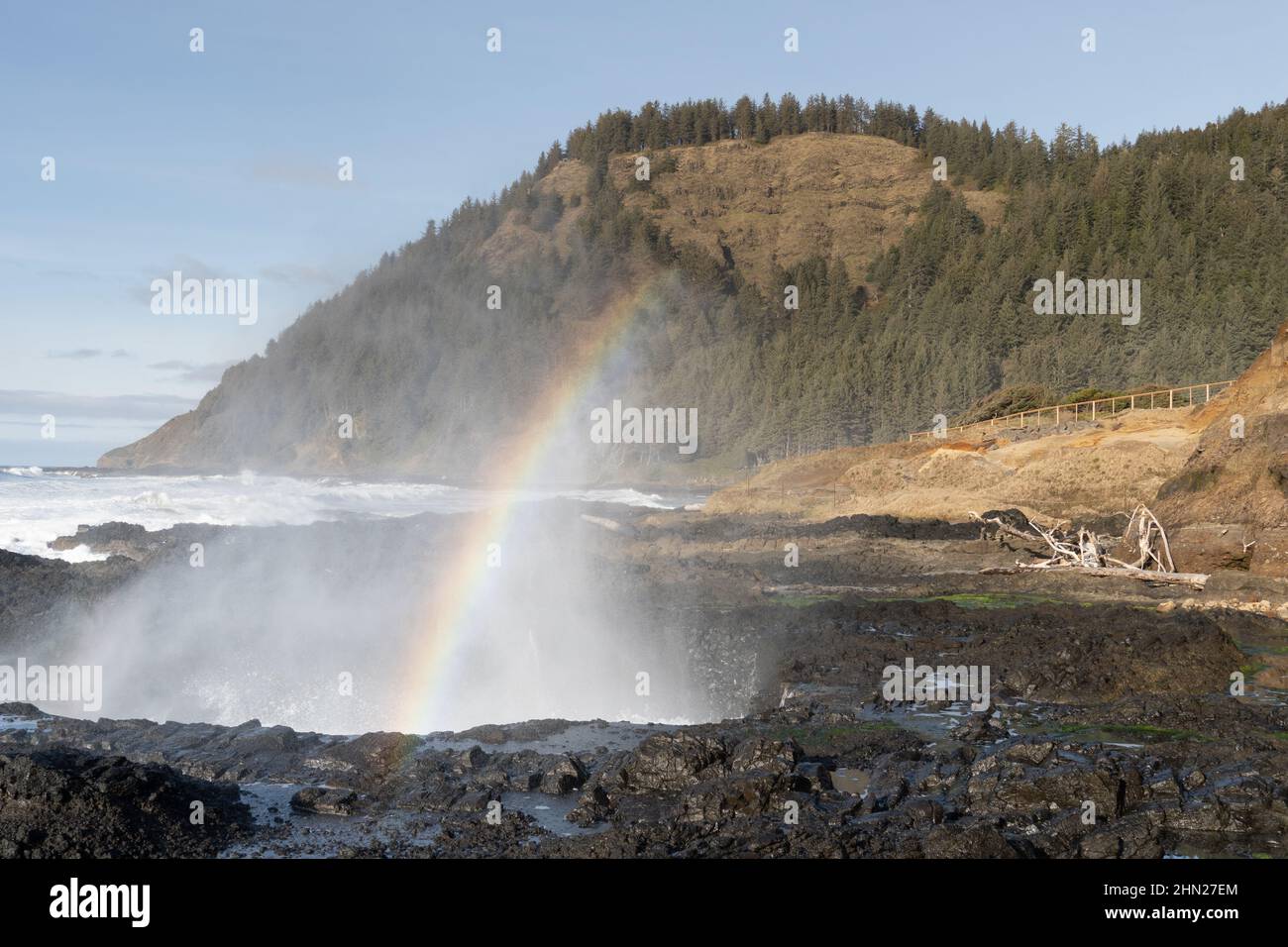 Rainbow e Ocean spray, formati come un'onda si scontra con una terrazza marina edificata. Capo Perpetua, Oregon, sullo sfondo. USA Foto Stock