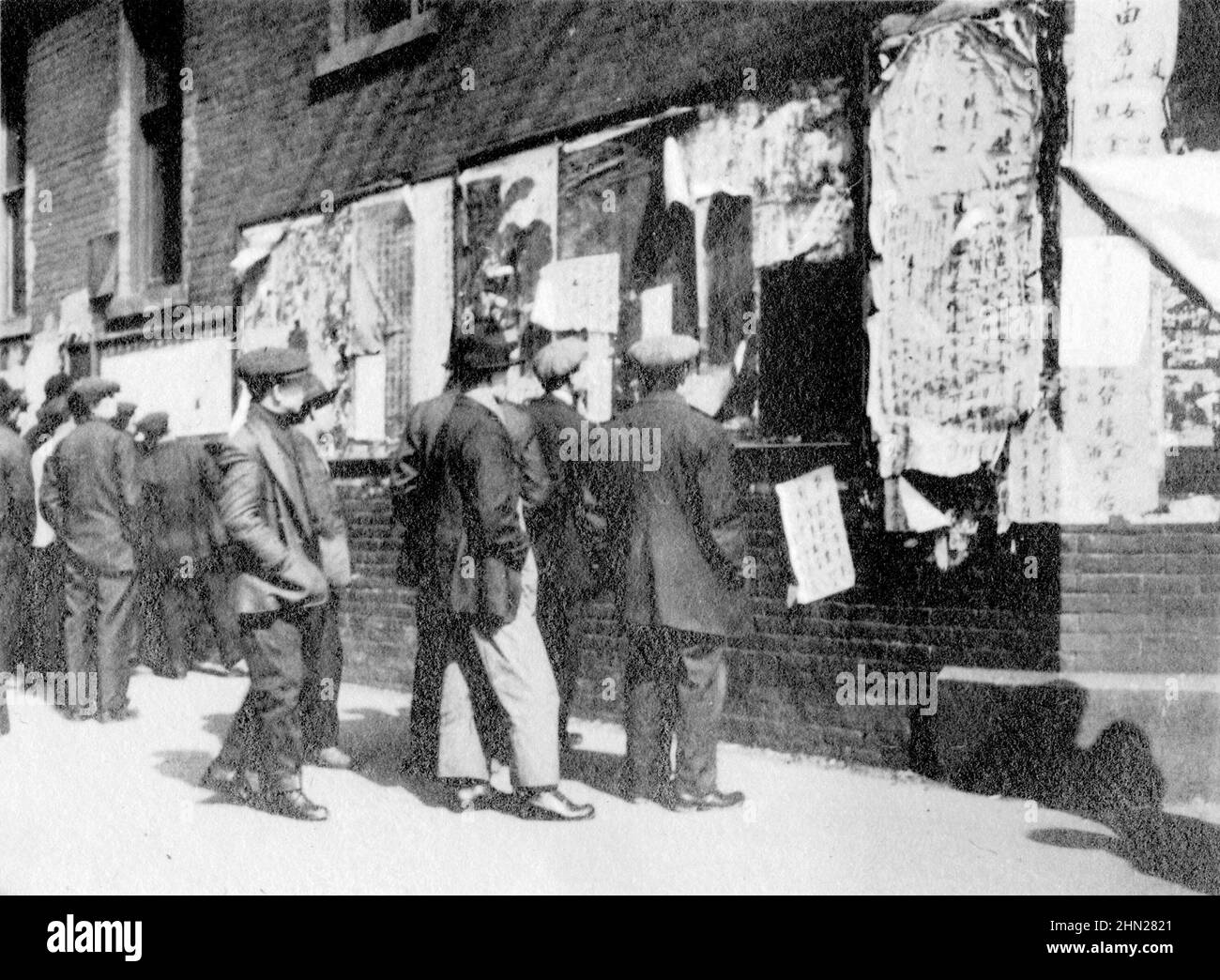 Fotografia vintage in bianco e nero ca. 1918 uomini cinesi che leggono giornali pubblicati sul muro di un edificio a Chinatown, Vancouver, Columbia Britannica, Canada Foto Stock