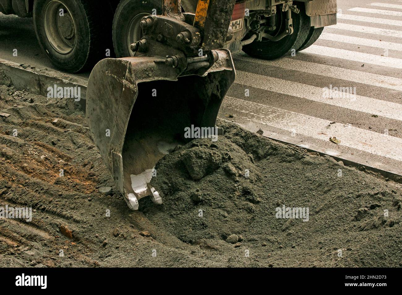 Lavori stradali sulla strada della città. La benna dell'escavatore raccoglie la vecchia pavimentazione e la carica in un dumper. Foto Stock