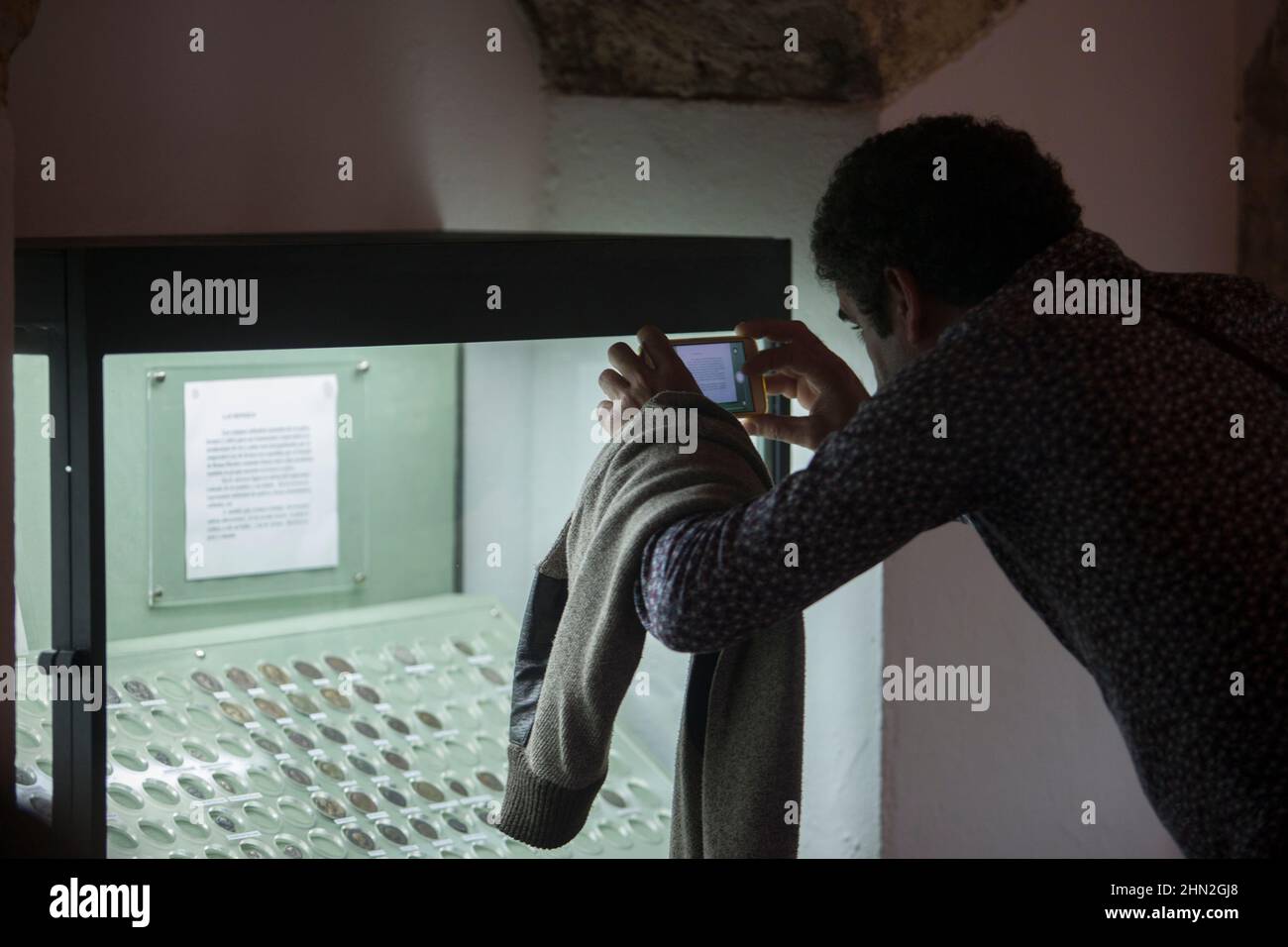 Visitatore che scatta foto all'antico armadietto di vetro delle monete. Museo Archeologico di Osuna, Siviglia Foto Stock