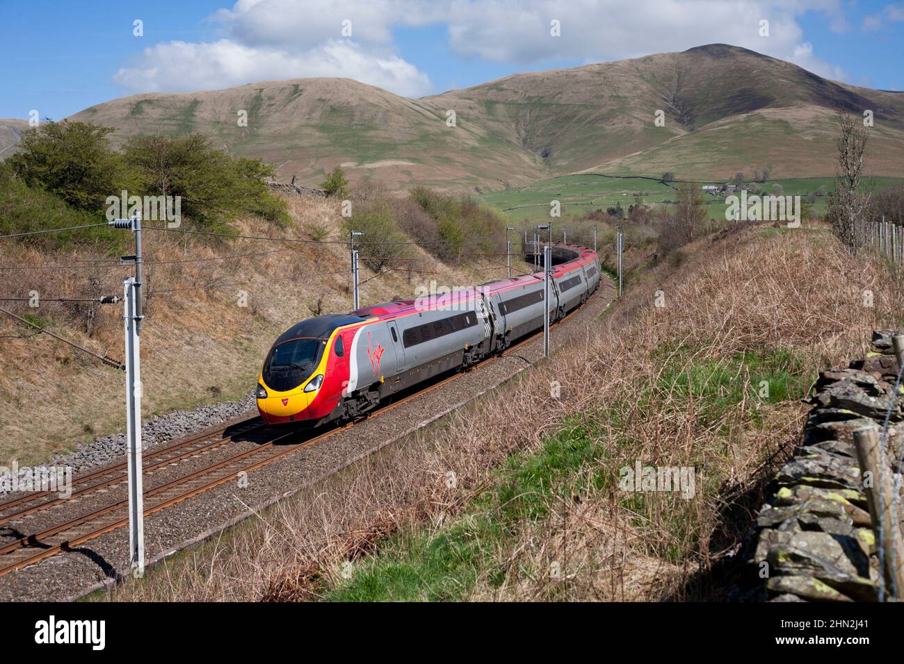 Virgin Trains Alstom Pendolino trenino 390132 nella campagna della Cumbria sulla linea principale elettrificata della costa occidentale, inclinando dietro un angolo Foto Stock