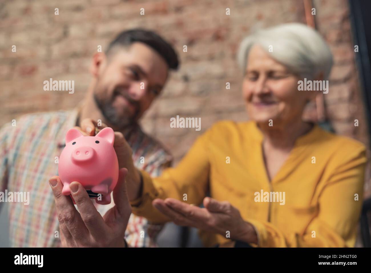 un uomo d'affari caucasico di successo che impara la sua nonna per risparmiare denaro usando la banca di piggy. Foto di alta qualità Foto Stock