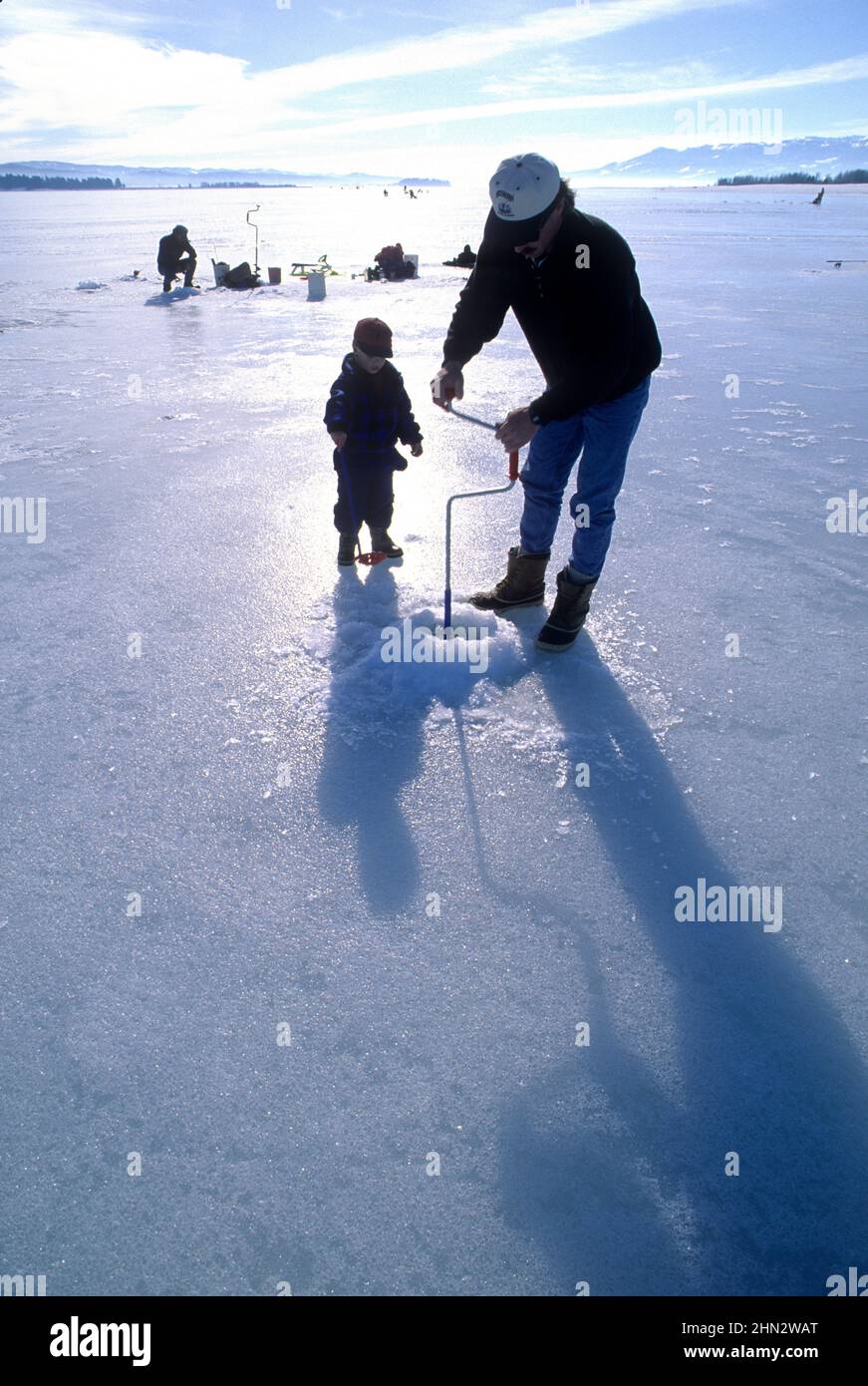 Uomo e 3-anno-vecchio ragazzo foro di perforazione in ghiaccio per la pesca sul ghiaccio al serbatoio a cascata, Idaho Foto Stock
