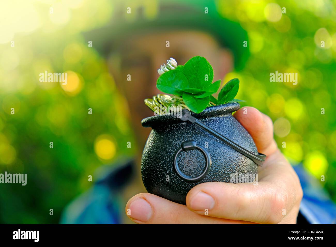 Saint Patrick .Clover foglia in cappello bowler con monete d'oro in mano di un uomo in un cappello verde in un soleggiato giardino.quadrifoglio trifoglio. Simbolo di buona fortuna Foto Stock